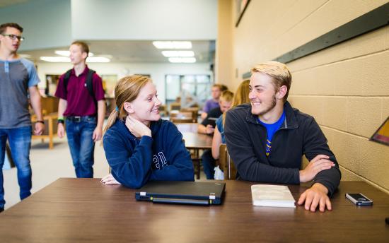 Students seated at a table at M State smile at each other